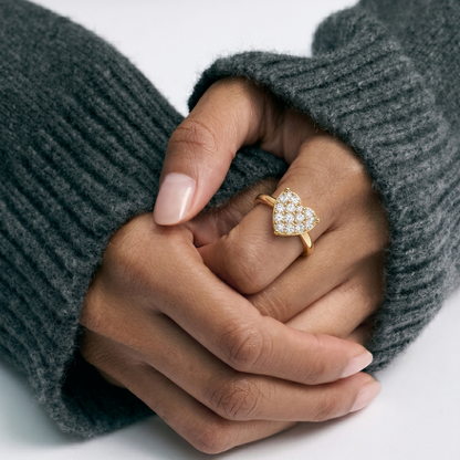 Hand wearing a gold heart-shaped diamond ring with gray sweater sleeves.