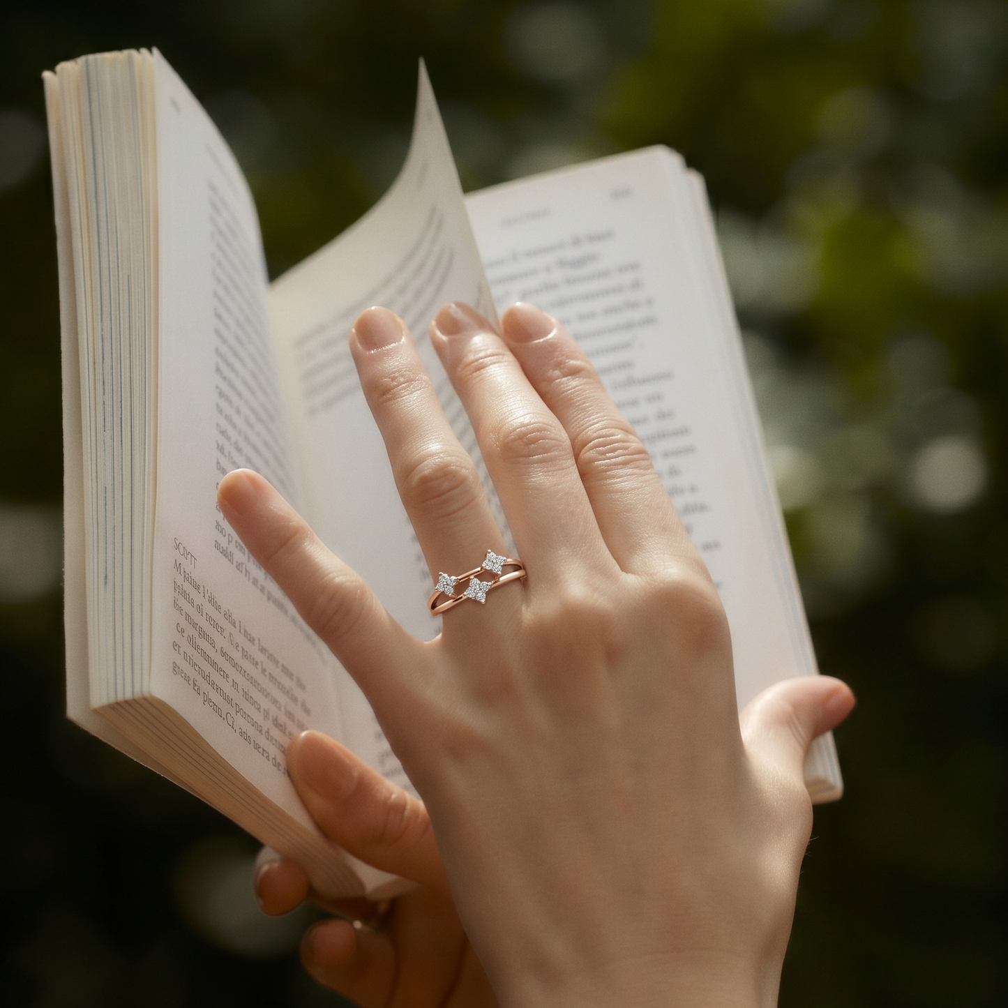 Hand holding an open book with a star-shaped ring on a blurred natural background
