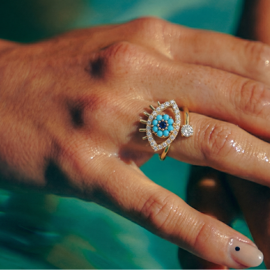 Close-up of a hand wearing an ornate ring with a blue gemstone against a blurred background