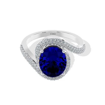 Elegant white gold ring featuring an oval blue gemstone with a twisted diamond-pavé band, photographed on a white background.