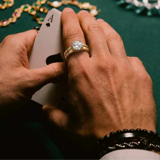 Hand holding a playing card with a diamond ring on a green surface with jewelry.