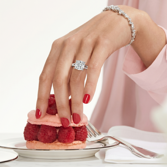 Hand with a diamond ring on a raspberry tart, wearing a pink dress.