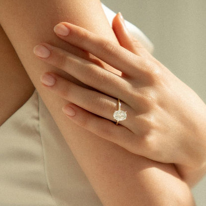 Hand wearing a oval diamond ring on a neutral background