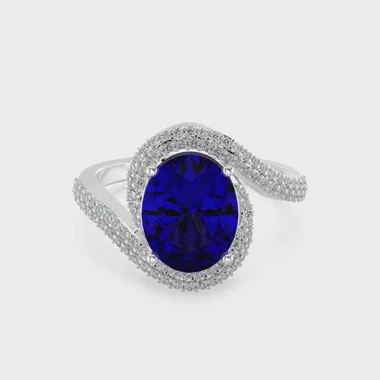 Elegant white gold ring featuring an oval blue gemstone with a twisted diamond-pavé band, photographed on a white background.