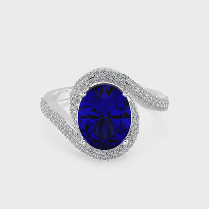 Elegant white gold ring featuring an oval blue gemstone with a twisted diamond-pavé band, photographed on a white background.